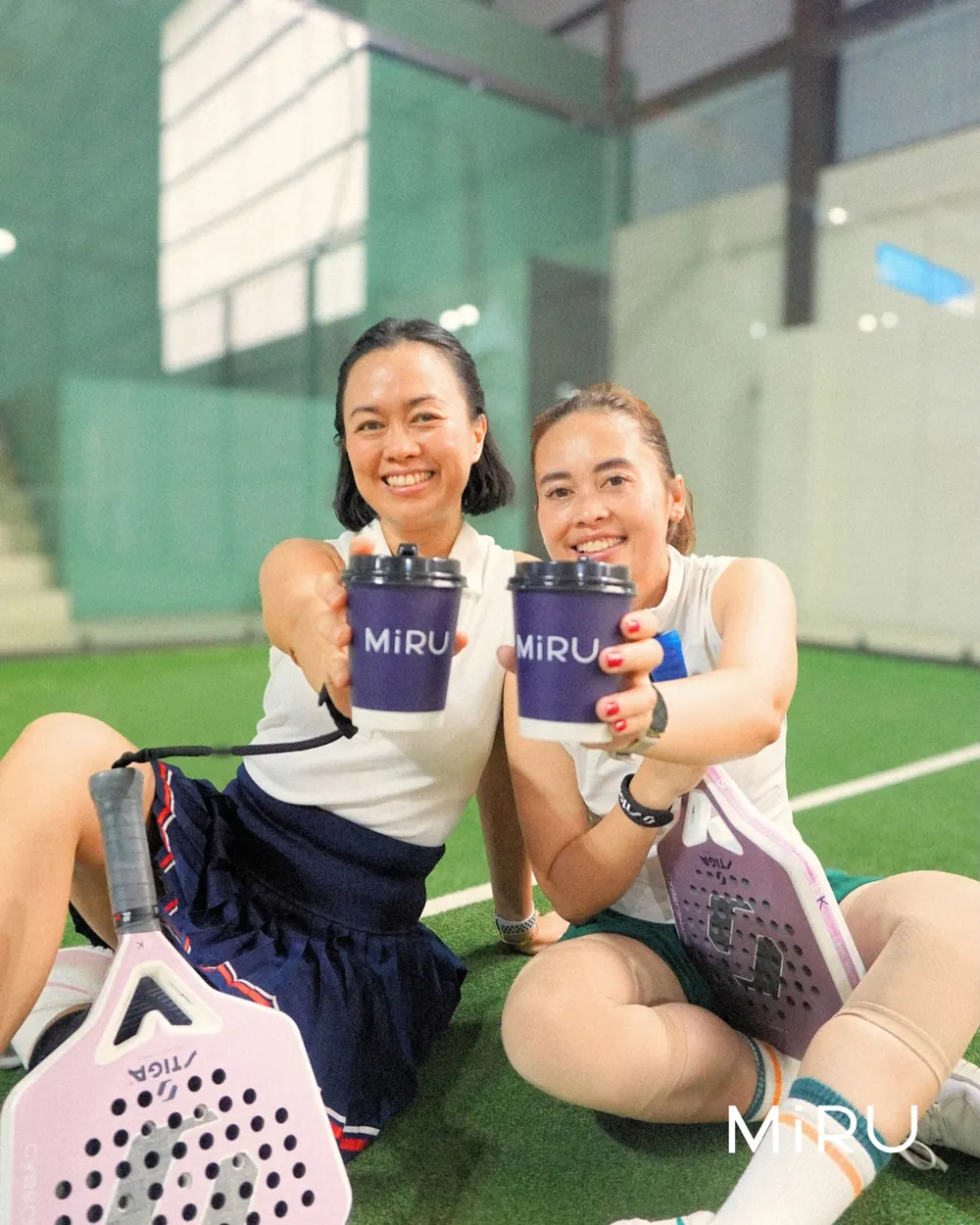 Two players sitting on the court, raising their Miru coffee cups