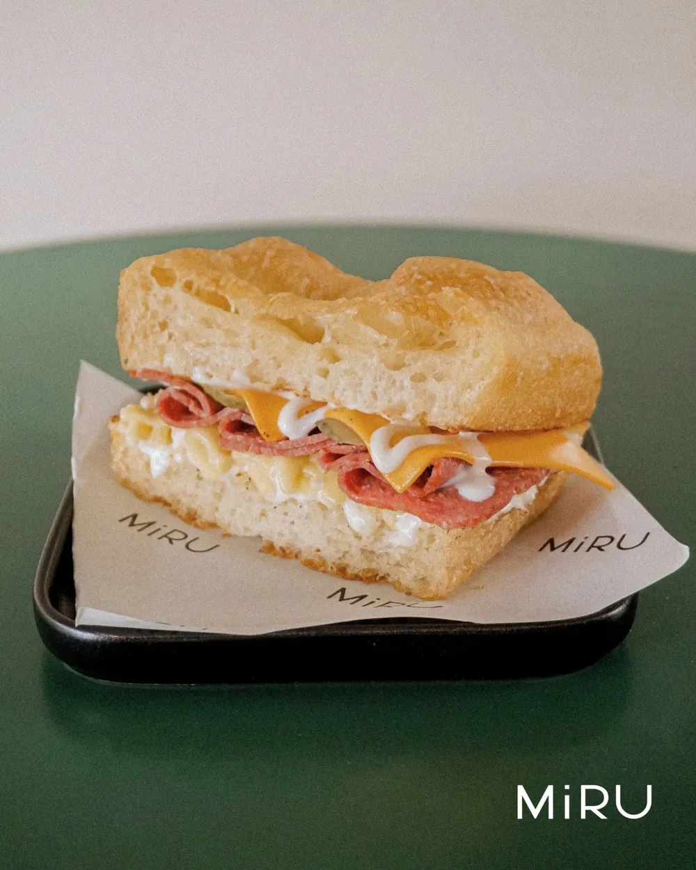 A focaccia sandwich layered with salami and cheese on a Miru tray