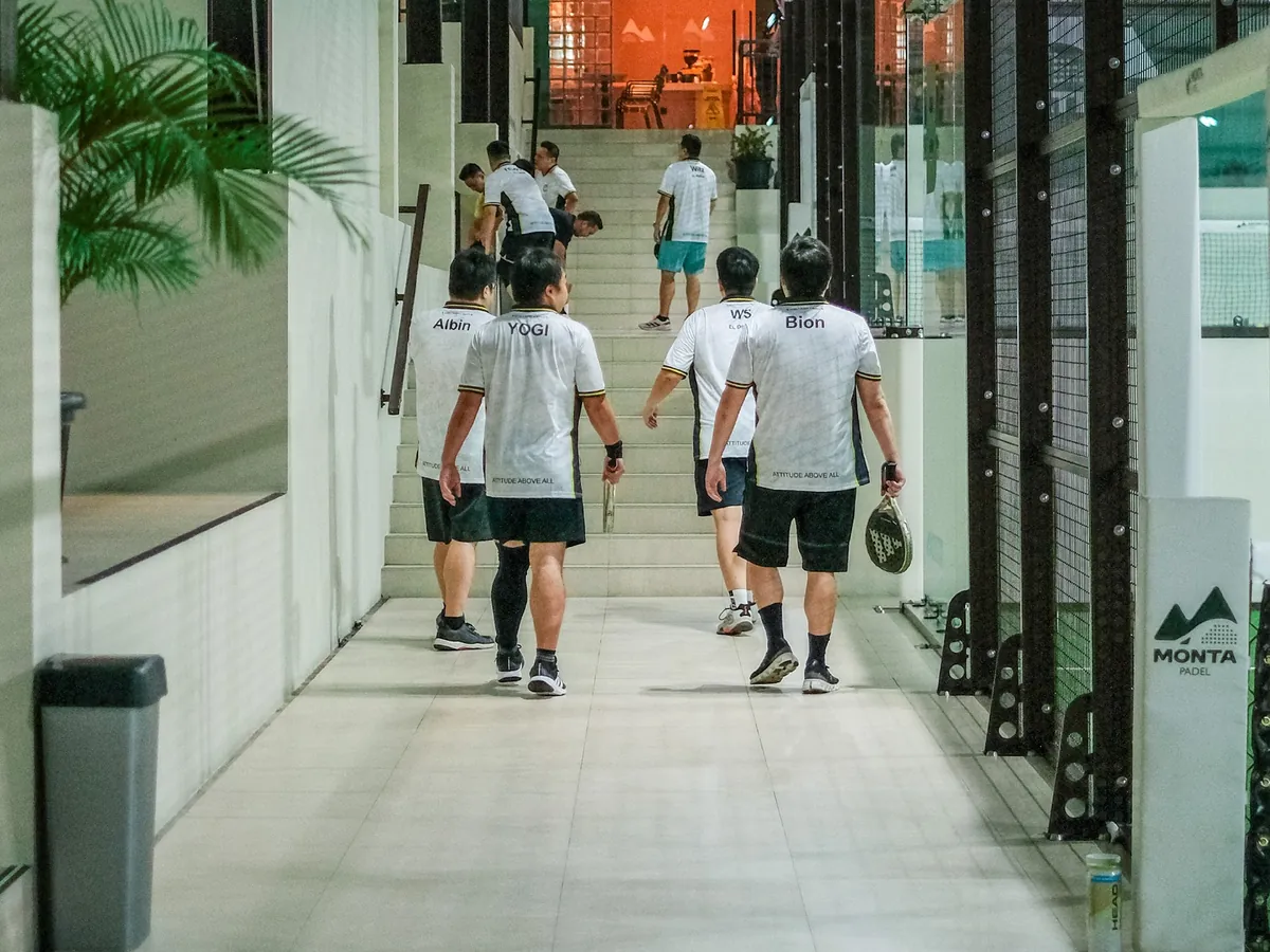 Players with rackets walking along the white corridor between the courts toward the stairs